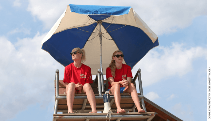 Two lifeguards sitting in a chair under an umbrella