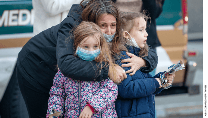 A mother wearing a mask holds her two children outside of NYU Langone Health hospital during the nightly "Clap Because We Care" cheer for medical staff and essential workers.